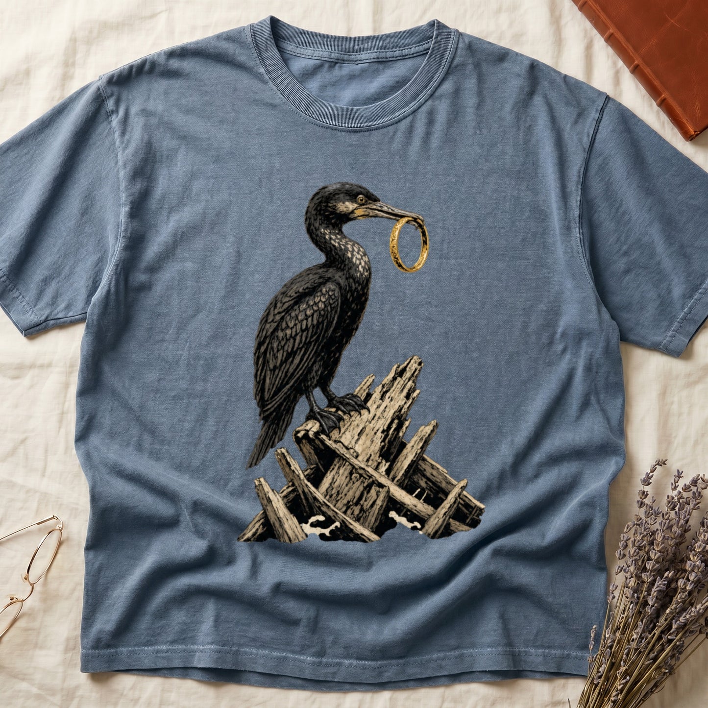 Blue t-shirt with graphic of cormorant holding a ring on a pile of driftwood.