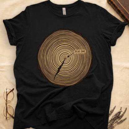 Black tee with cross-section of tree rings in warm brown, arrow pointing to center labeled "YEAR ONE" in serif type.