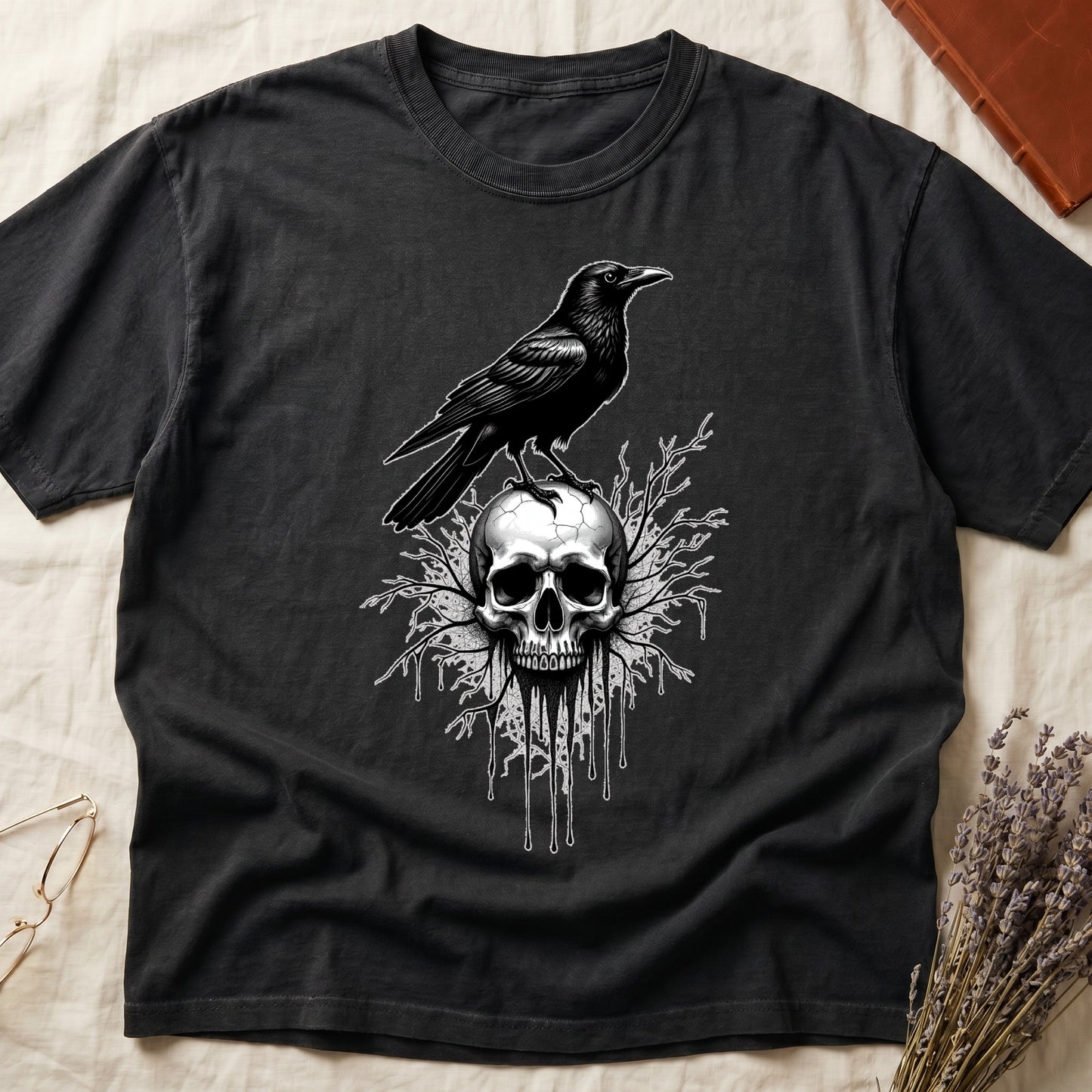 Black tee with raven silhouette on human skull, ink drips from jaw, bare branches behind, monochrome illustration.