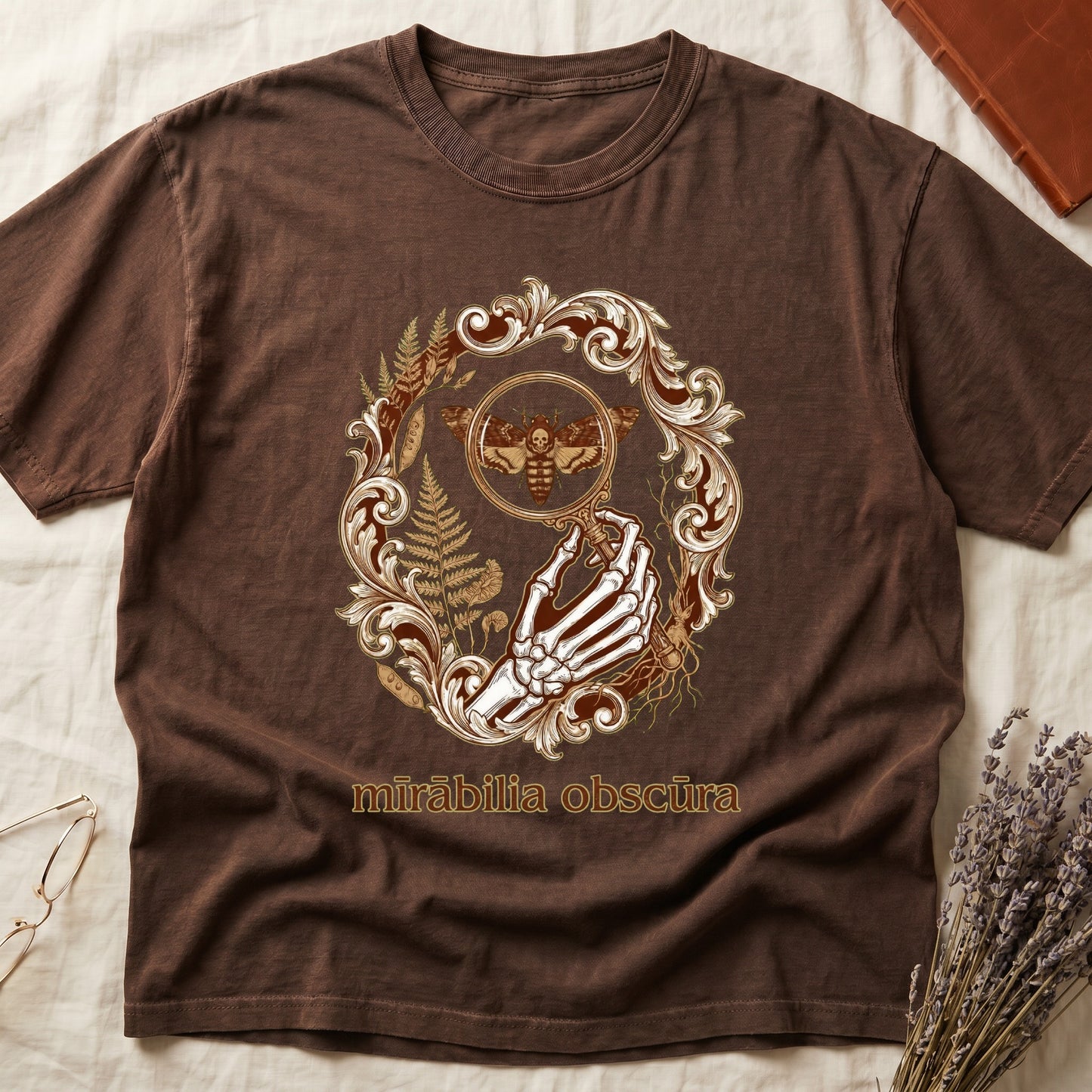 Espresso tee with skeletal hand, magnifying glass, death's-head moth, ferns on green, "mīrābilia obscūra" in Latin italic.