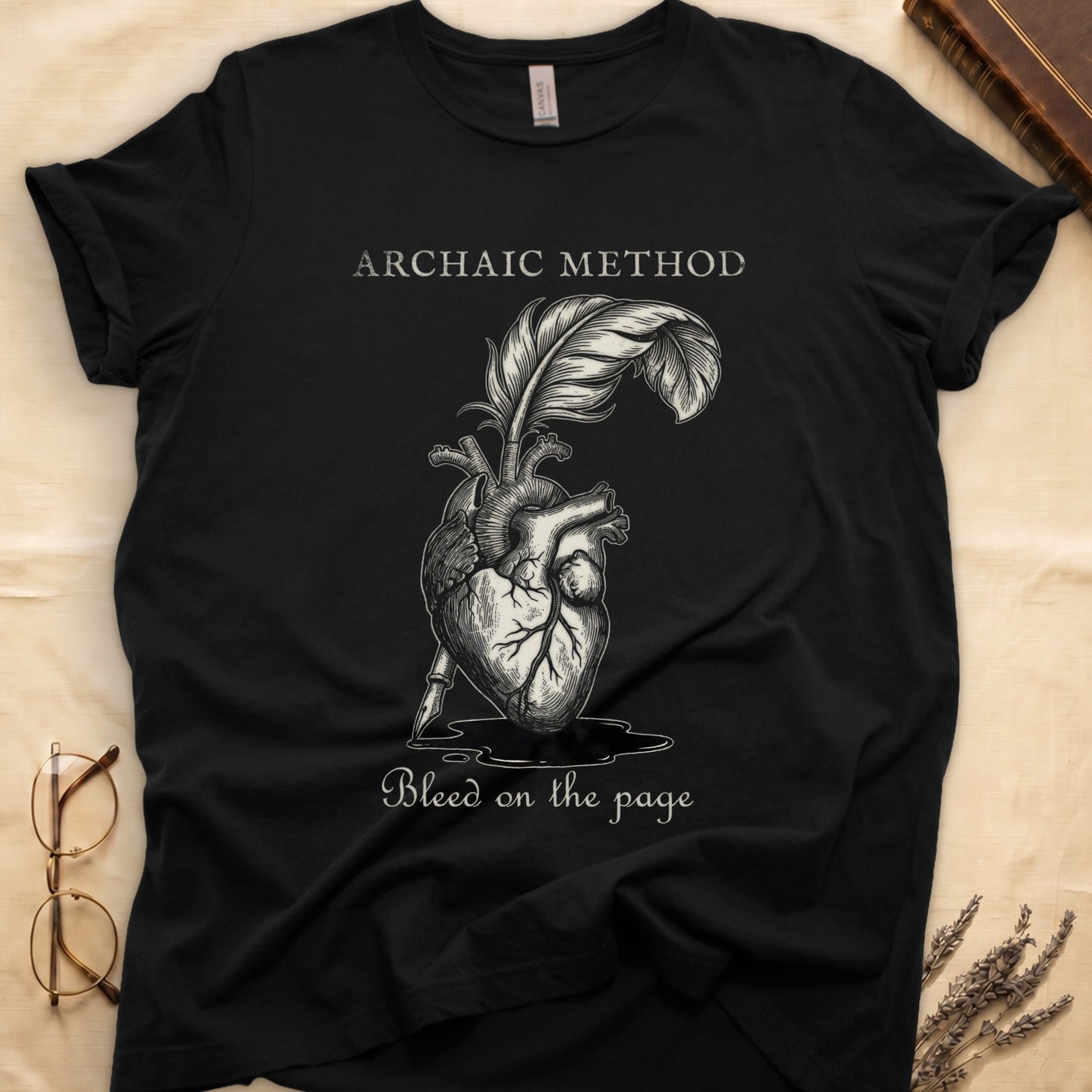 Black tee with anatomical heart and quill emerging in cream linework, "ARCHAIC METHOD" top, "Bleed on the page" below.