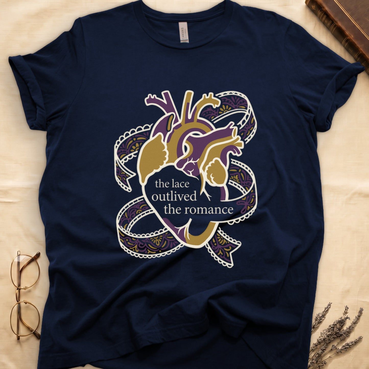 Navy tee with anatomical heart in purple and gold wrapped in lace ribbons, "the lace outlived the romance" in serif.