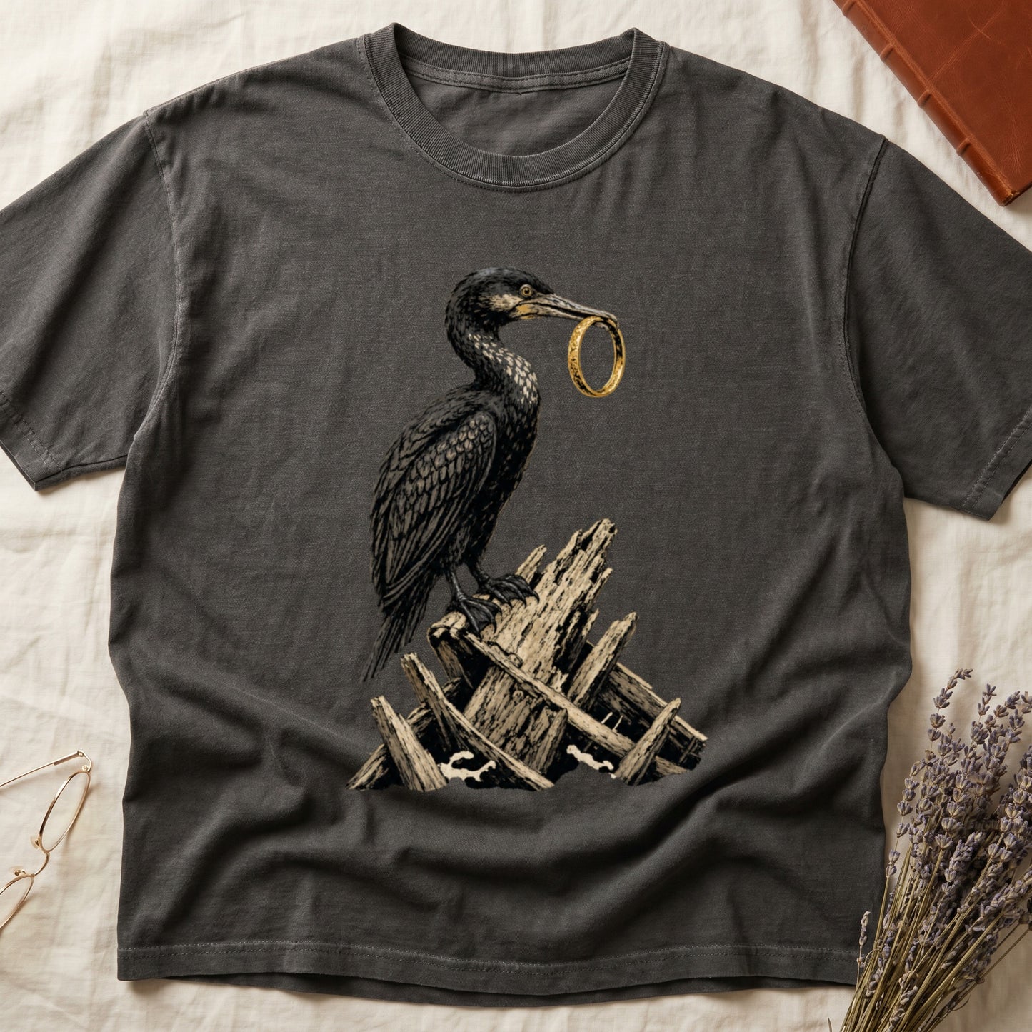 Dark t-shirt with a black bird holding a gold ring on a pile of wood.