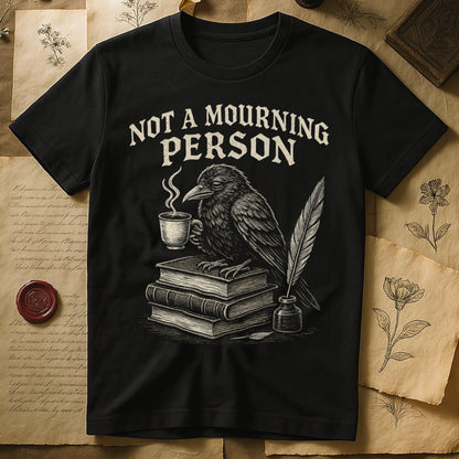 Black tee with raven holding coffee on stack of books, quill in inkwell, "NOT A MOURNING PERSON" distressed serif top.