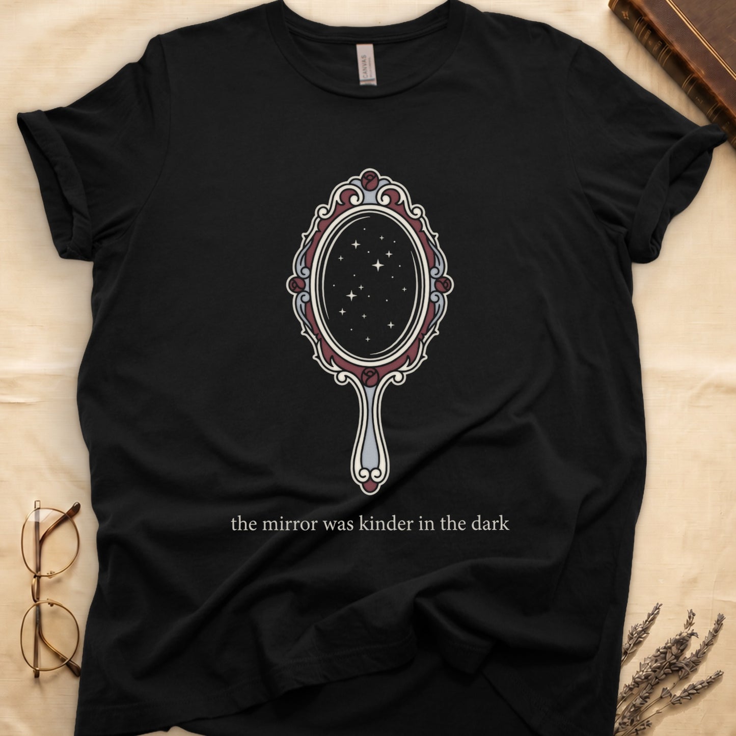 Black tee with ornate hand mirror, dark red roses, starfield reflection, "the mirror was kinder in the dark" serif below.