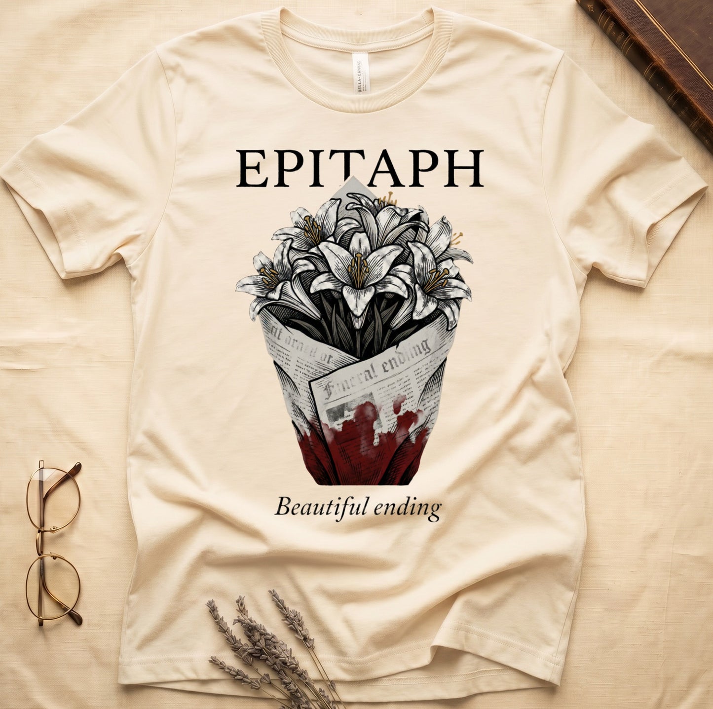 Natural tee with "EPITAPH" over crosshatched white lilies in blood-stained newsprint wrap, "Beautiful ending" italic serif.