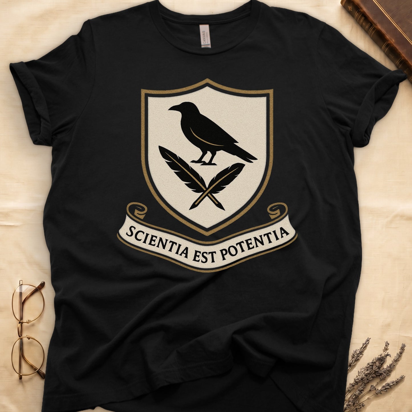 Black tee with cream-and-gold heraldic shield, black raven over crossed quills, scroll banner "SCIENTIA EST POTENTIA" below.