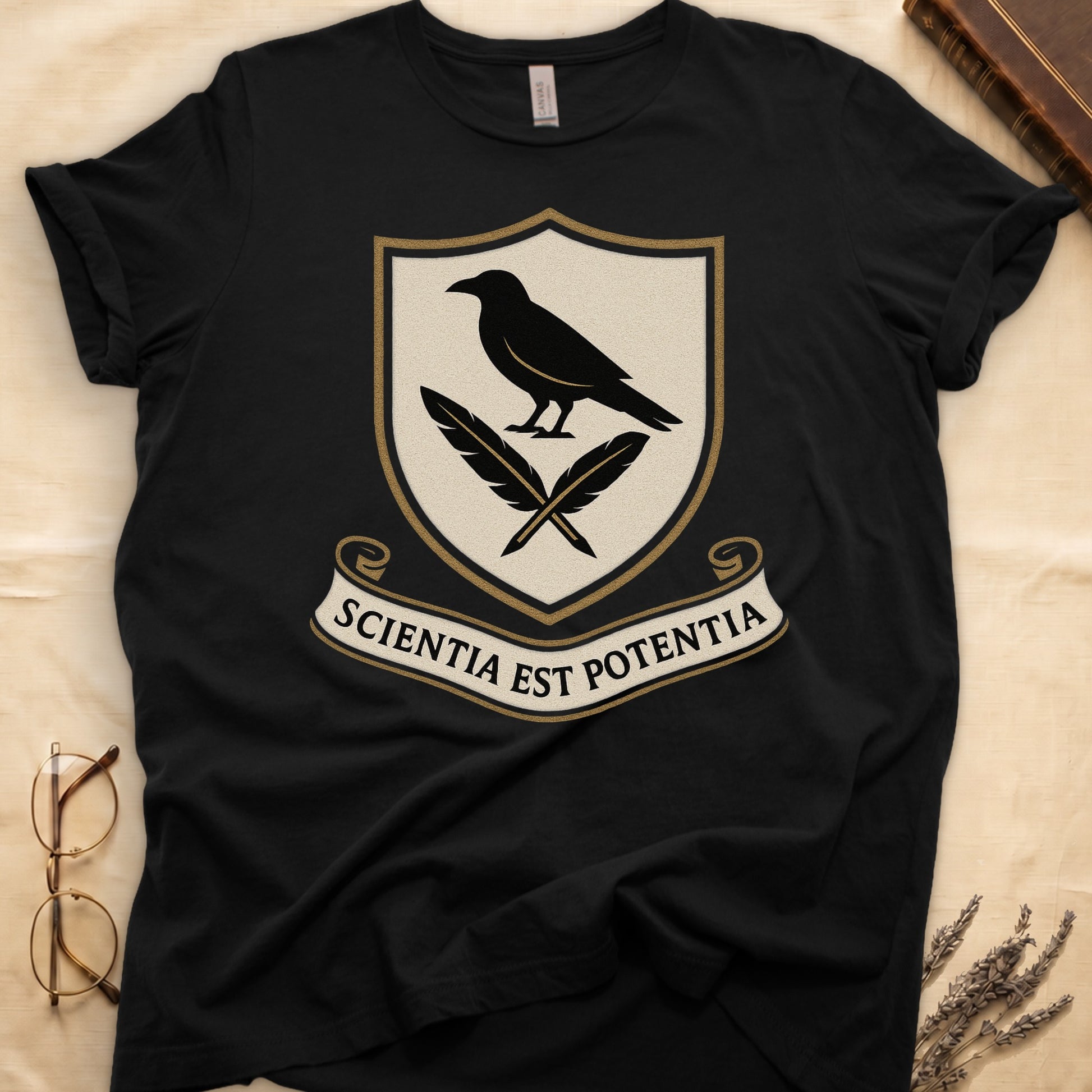 Black tee with cream-and-gold heraldic shield, black raven over crossed quills, scroll banner "SCIENTIA EST POTENTIA" below.
