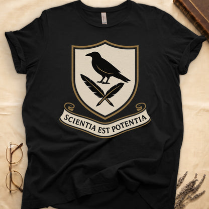 Black tee with cream-and-gold heraldic shield, black raven over crossed quills, scroll banner "SCIENTIA EST POTENTIA" below.