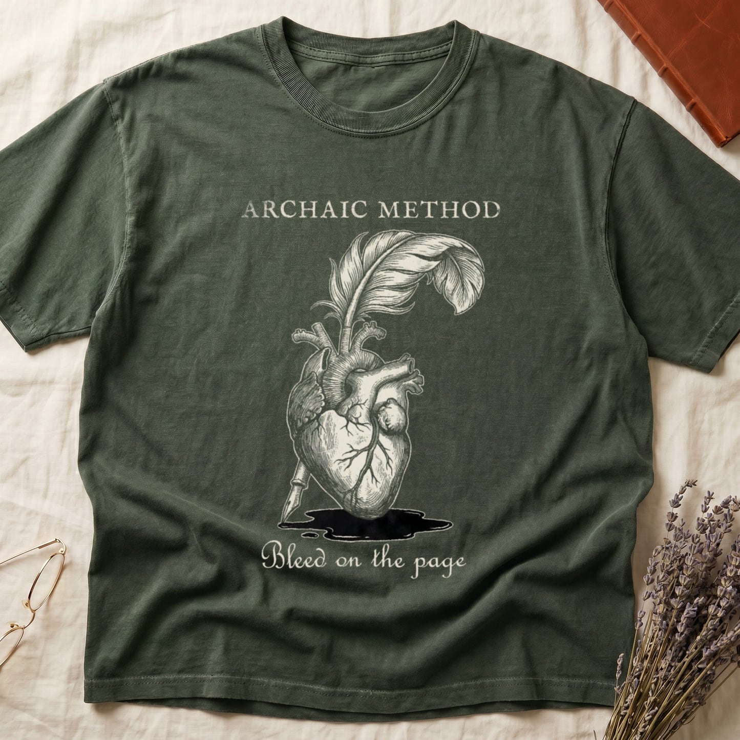 Green tee with anatomical heart and quill emerging in cream linework, "ARCHAIC METHOD" top, "Bleed on the page" below.