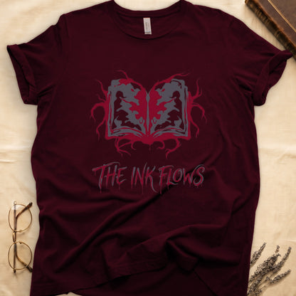 Maroon tee with open book bleeding red ink into a gray face on green ground, "THE INK FLOWS" in dripping serif.