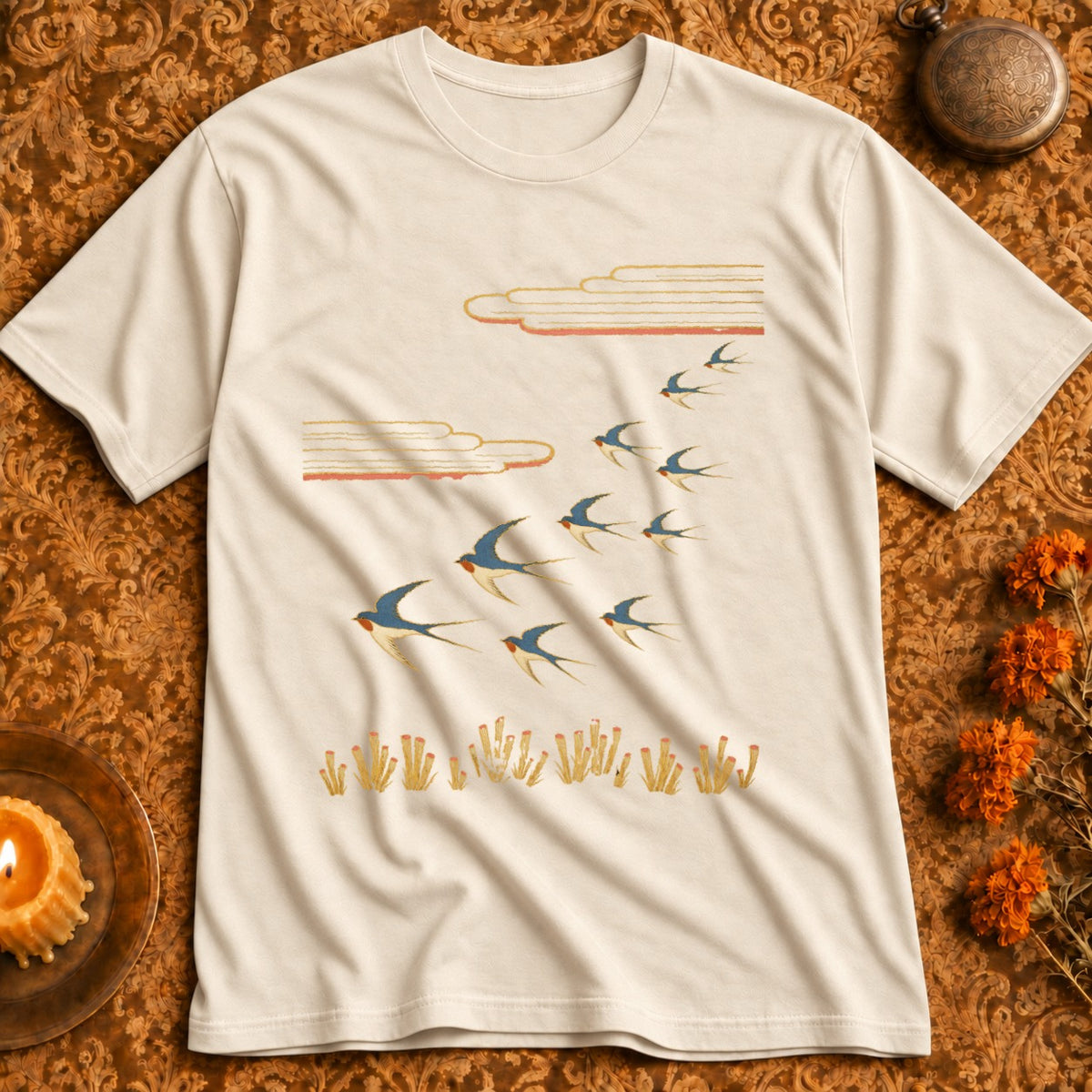 Cream t-shirt with a graphic of swallows flying over reeds under stylized clouds.
