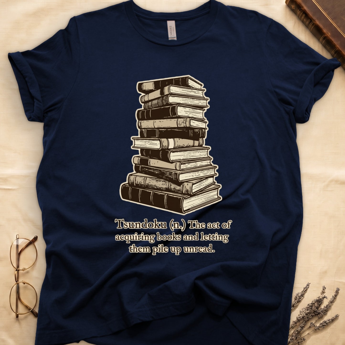 Navy tee with stack of vintage hardcovers, "Tsundoku (n.) The act of acquiring books and letting them pile up unread."
