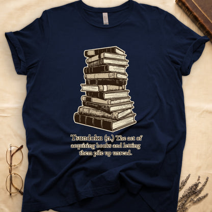 Navy tee with stack of vintage hardcovers, "Tsundoku (n.) The act of acquiring books and letting them pile up unread."