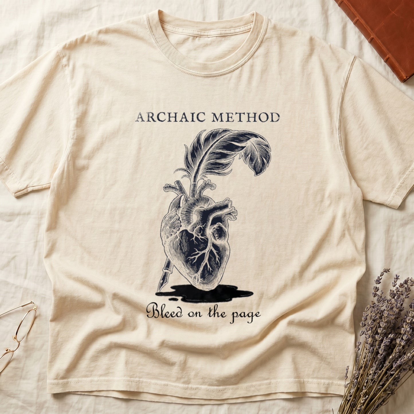 Ivory tee with anatomical heart and quill emerging in cream linework, "ARCHAIC METHOD" top, "Bleed on the page" below.
