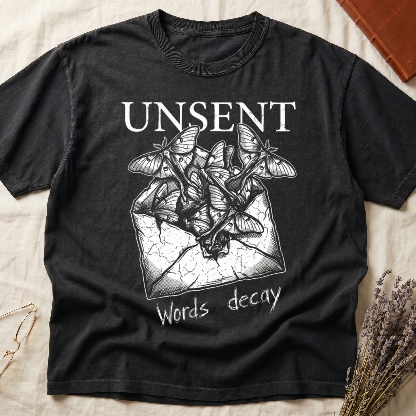 Black tee with 'UNSENT' in serif type, 'Words decay' brush text, luna moths from torn envelope in crosshatched ink