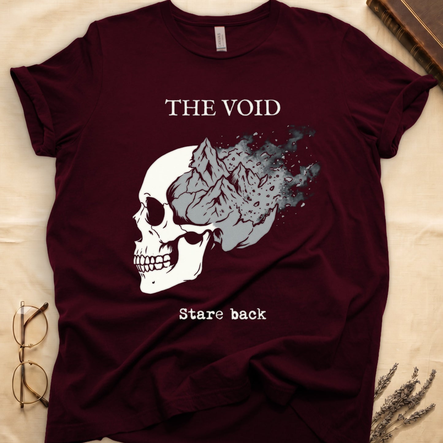 Maroon tee with skull eroding into mountain landscape and stardust, "THE VOID" top, "Stare back" typewriter below.
