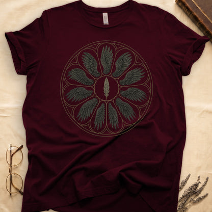 Maroon tee with sepia rose-window of eight feathered wings around central feather, engraved linework on parchment ground.