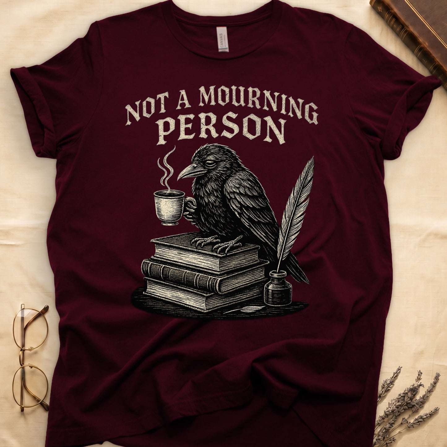 Navy tee with raven holding coffee on stack of books, quill in inkwell, "NOT A MOURNING PERSON" distressed serif top.