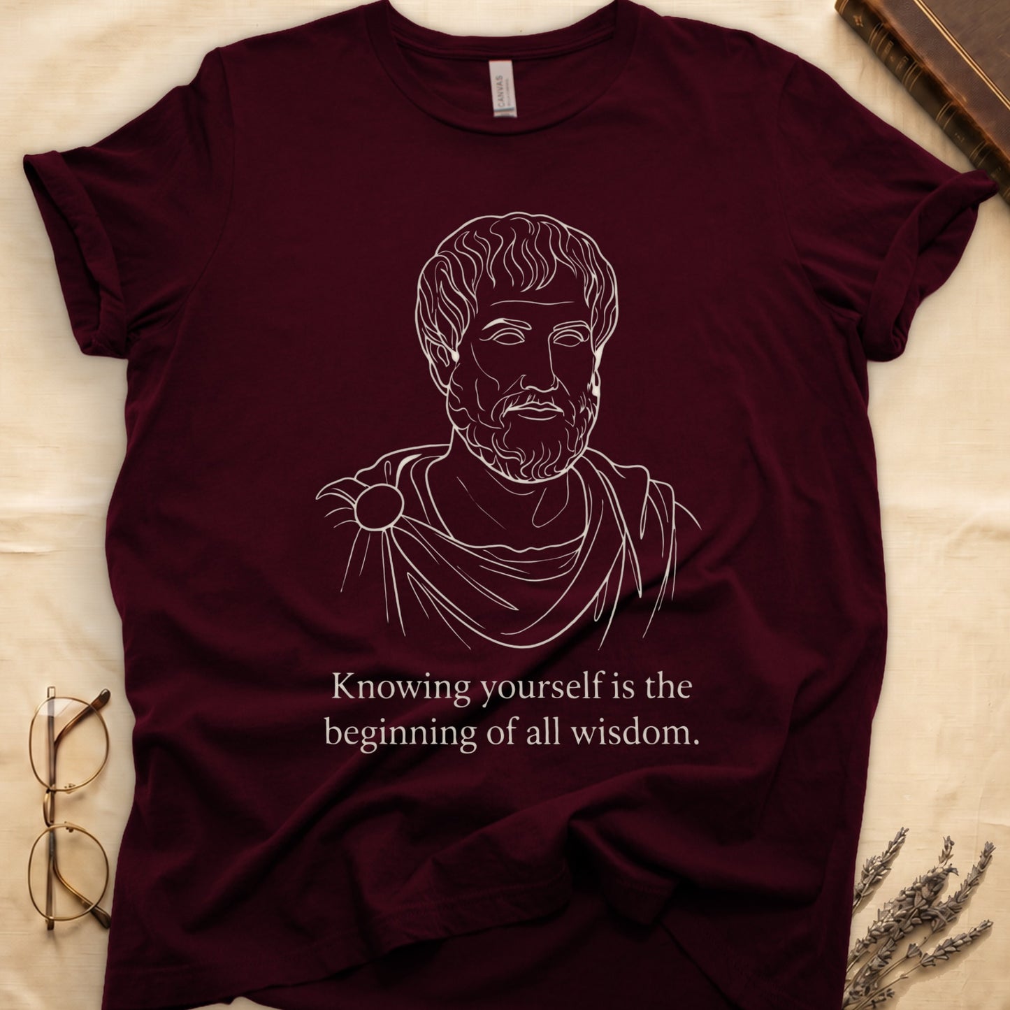 Maroon tee with classical philosopher bust in cream linework, "Knowing yourself is the beginning of all wisdom" below.