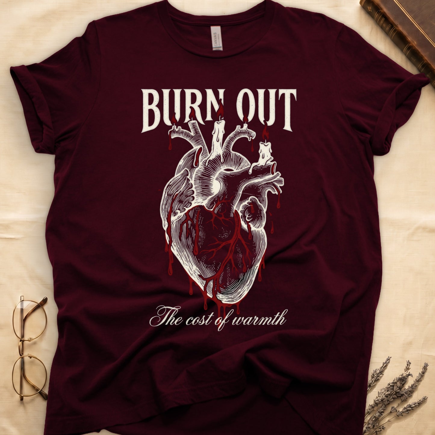 Maroon tee with anatomical heart and melted candles dripping red wax, "BURN OUT" top, "The cost of warmth" cursive below.