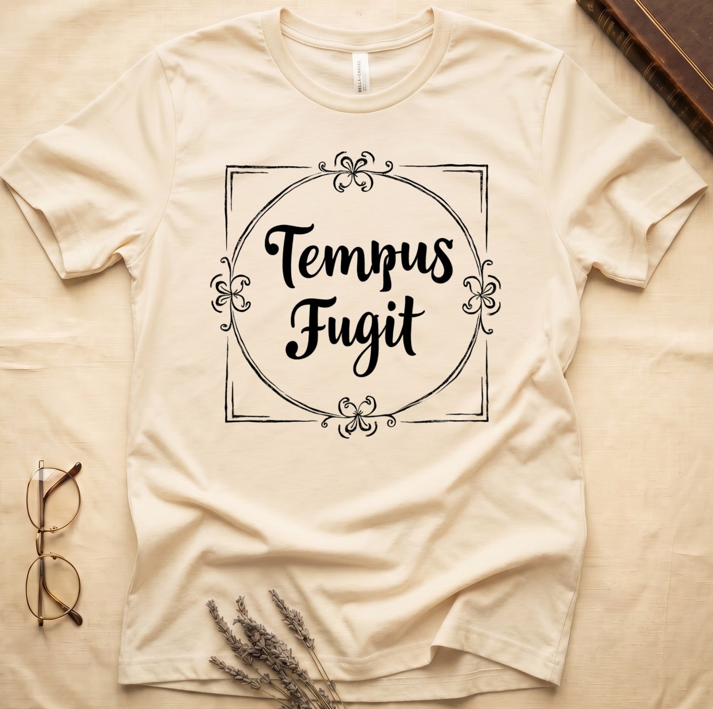 Natural tee with cream "Tempus Fugit" script inside square filigree frame, decorative corner flourishes, classical typography.