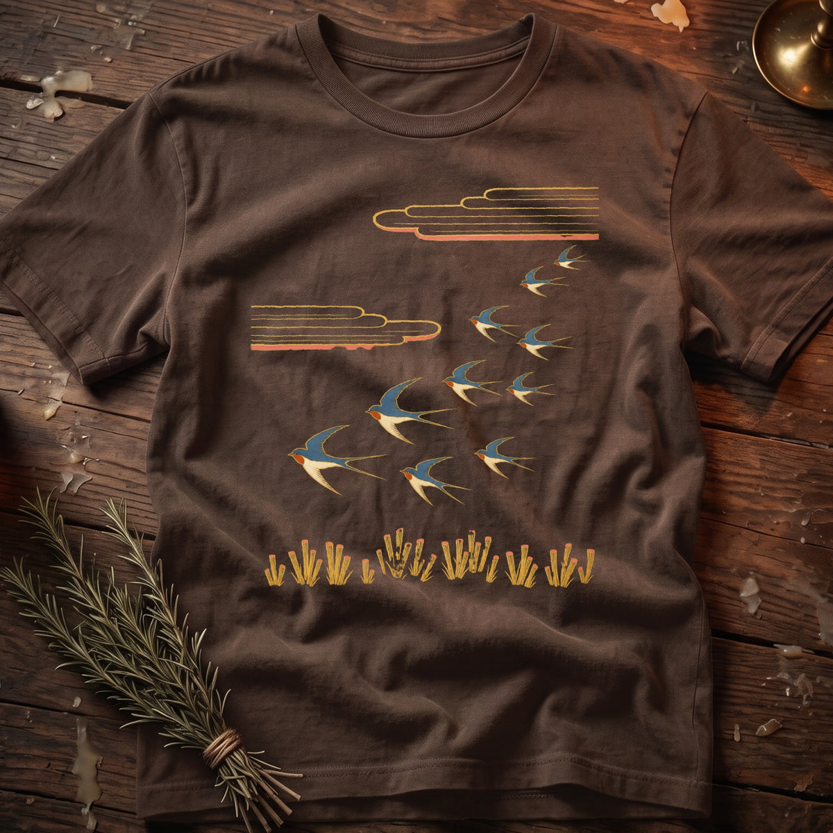Brown t-shirt with a graphic of swallows flying under stylized clouds above yellow grass.