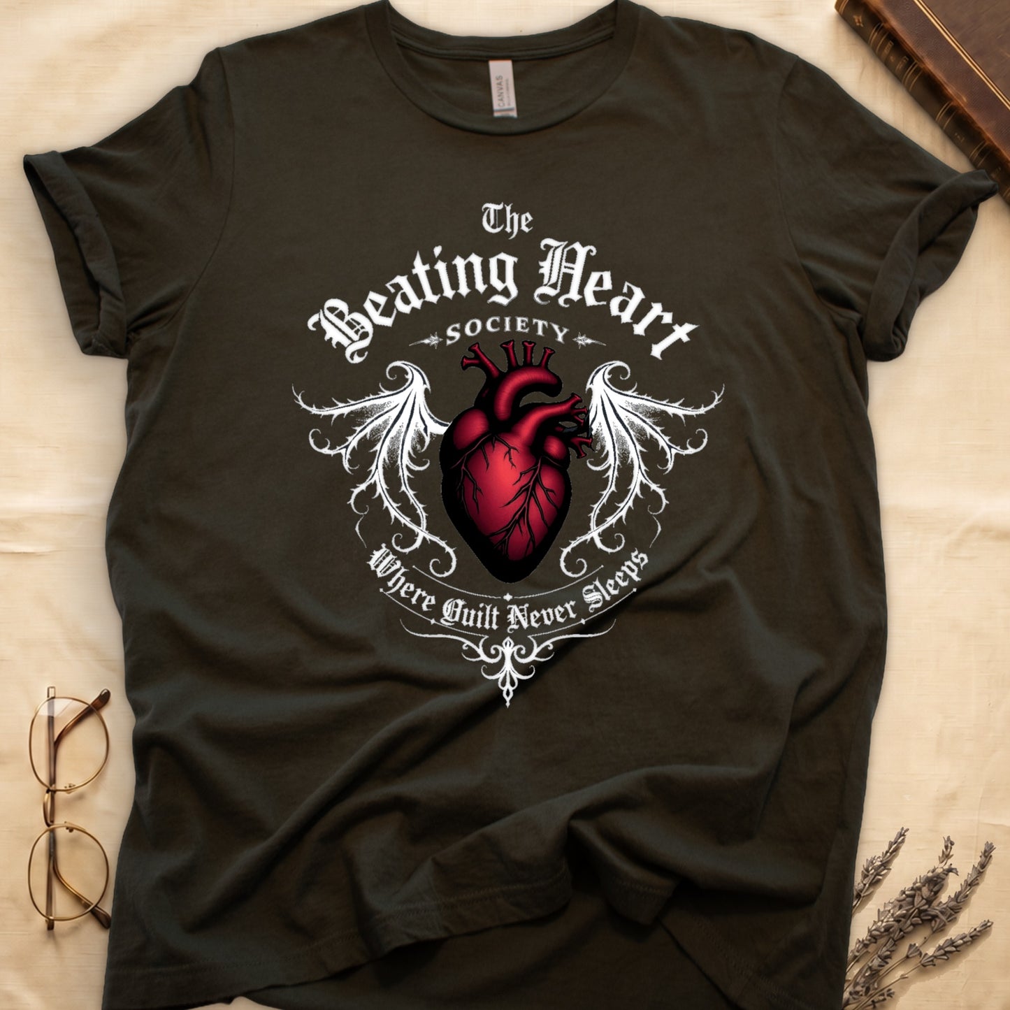 Military Green tee with anatomical red heart, gothic wings, "The Beating Heart SOCIETY," "Where Guilt Never Sleeps" below.