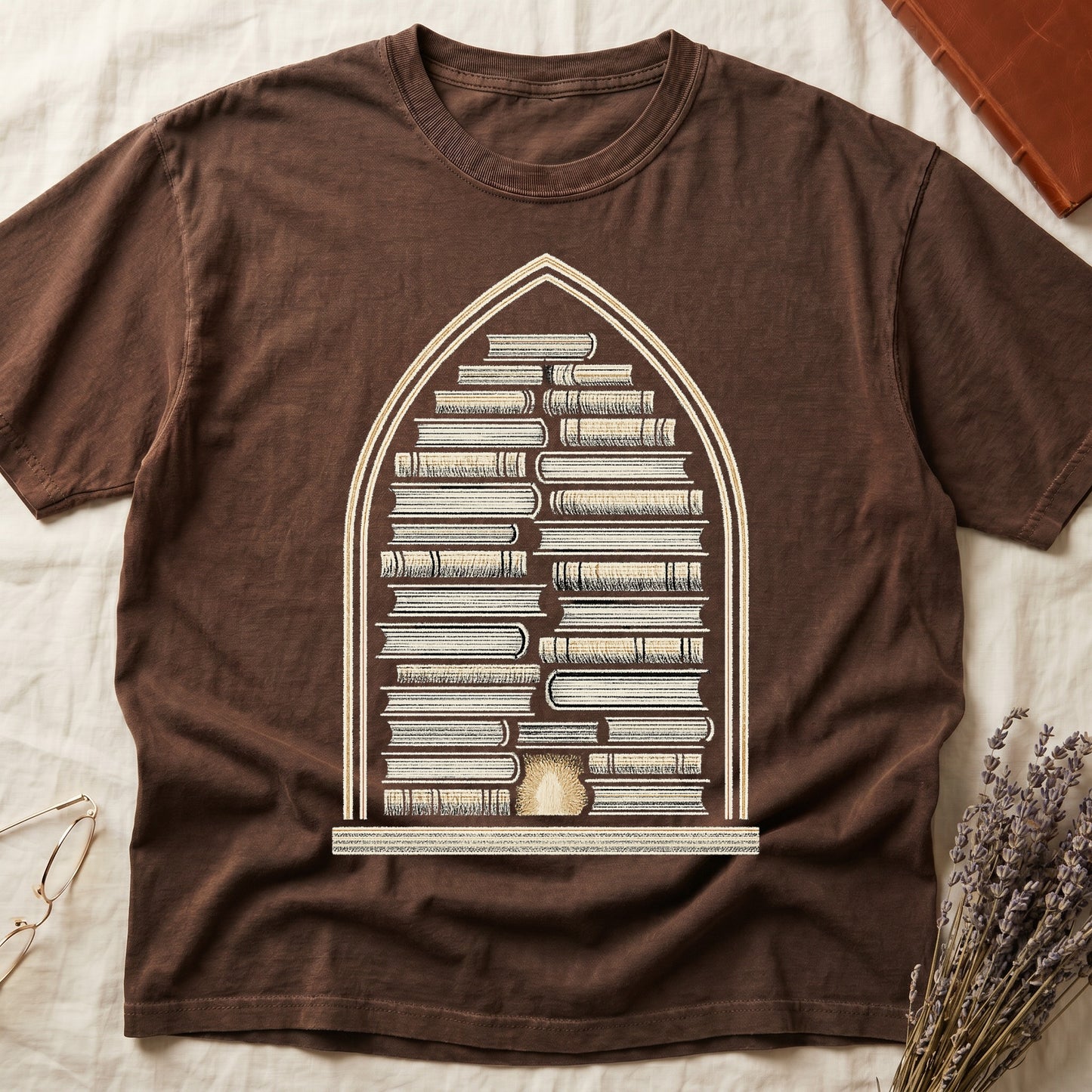 Espresso tee with gothic arch frame, columns of leather-bound books inside, sunburst medallion at base, cream engraved linework.