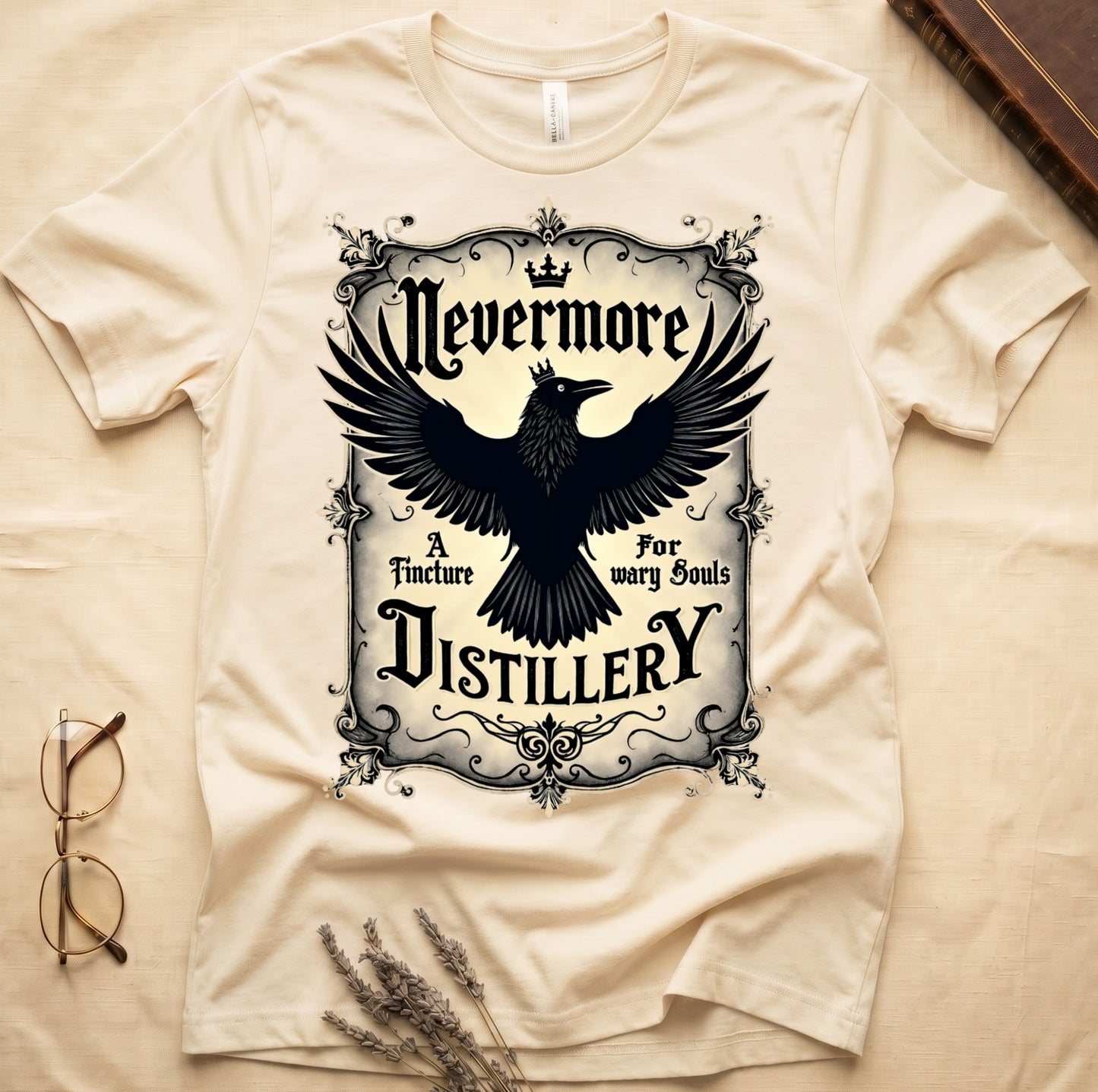 Natural tee with antique label, crowned raven, blackletter "Nevermore" top, "A Tincture For wary Souls," "DISTILLERY" bottom.