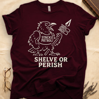 Maroon tee with vintage raven mascot, "STACKS PATROL" sash, feather pen aloft, "SHELVE OR PERISH" bold serif below.