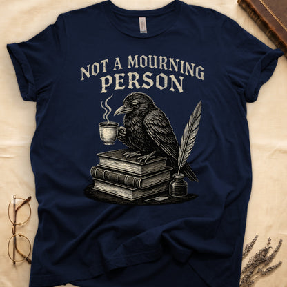 Black tee with raven holding coffee on stack of books, quill in inkwell, "NOT A MOURNING PERSON" distressed serif top.