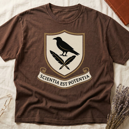 Espresso tee with cream-and-gold heraldic shield, black raven over crossed quills, scroll banner "SCIENTIA EST POTENTIA" below.
