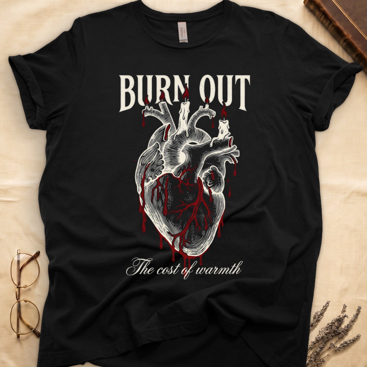 Black tee with anatomical heart and melted candles dripping red wax, "BURN OUT" top, "The cost of warmth" cursive below.