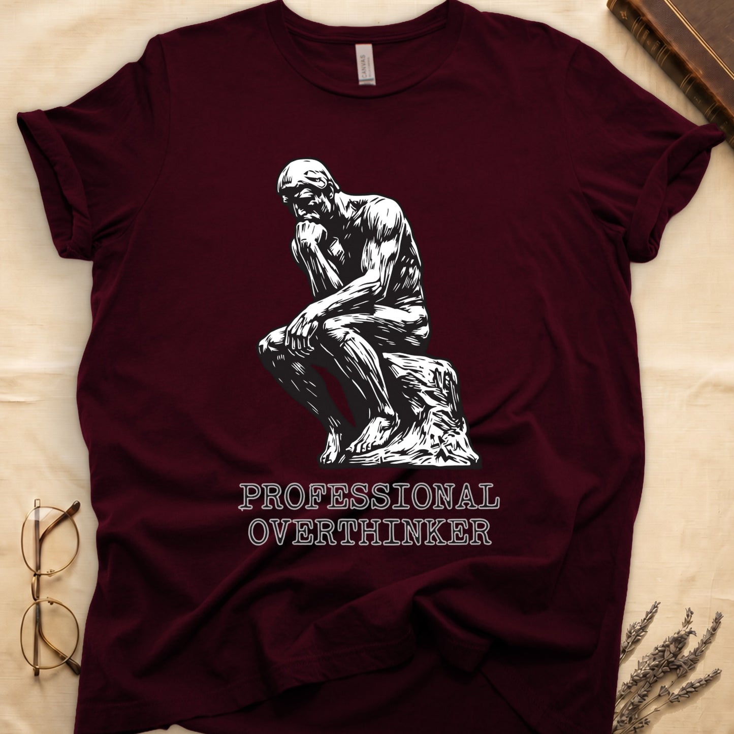 Maroon tee with monochrome rendering of Rodin's Thinker, "PROFESSIONAL OVERTHINKER" in serif capitals below.
