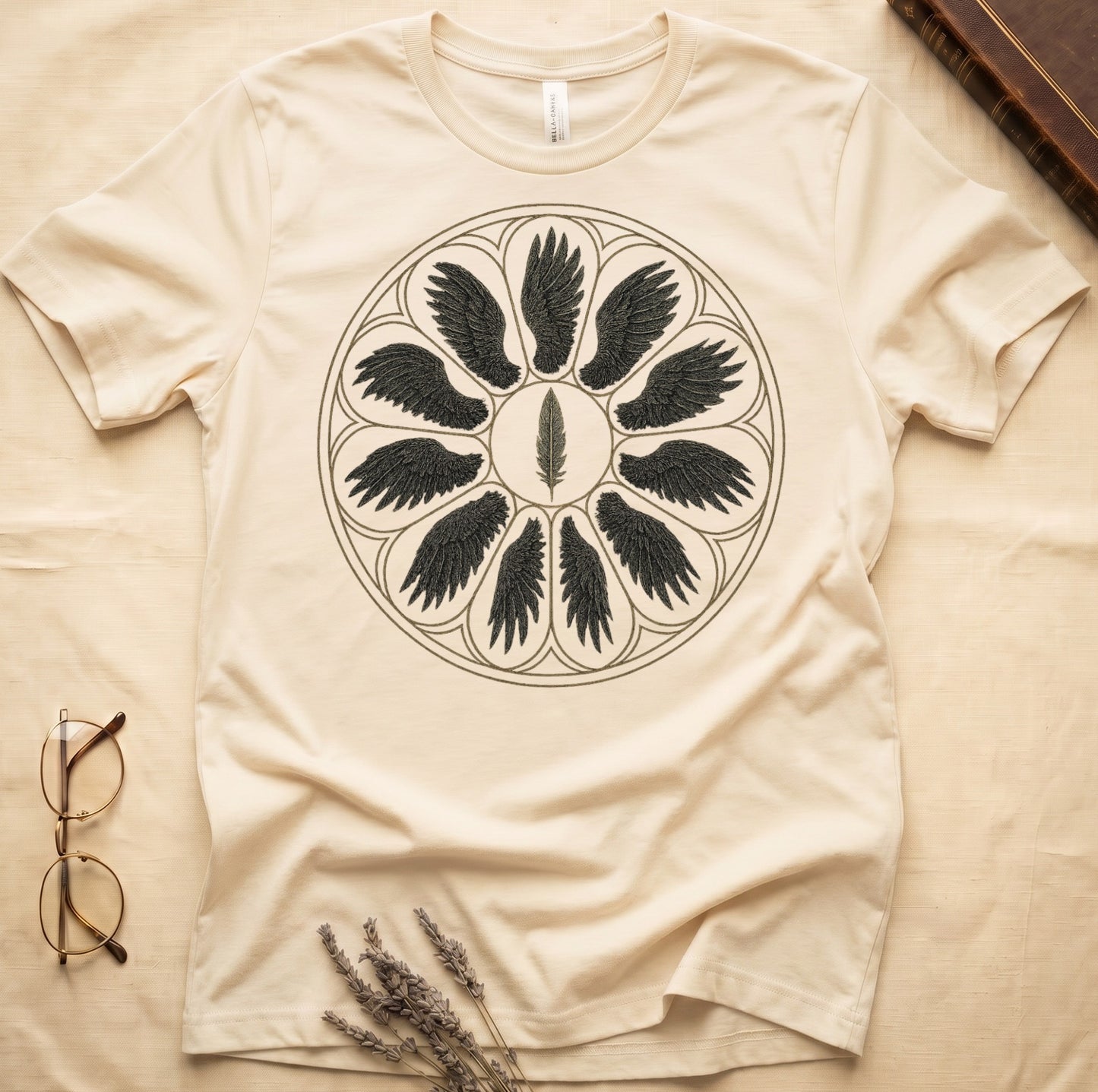 Natural tee with sepia rose-window of eight feathered wings around central feather, engraved linework on parchment ground.