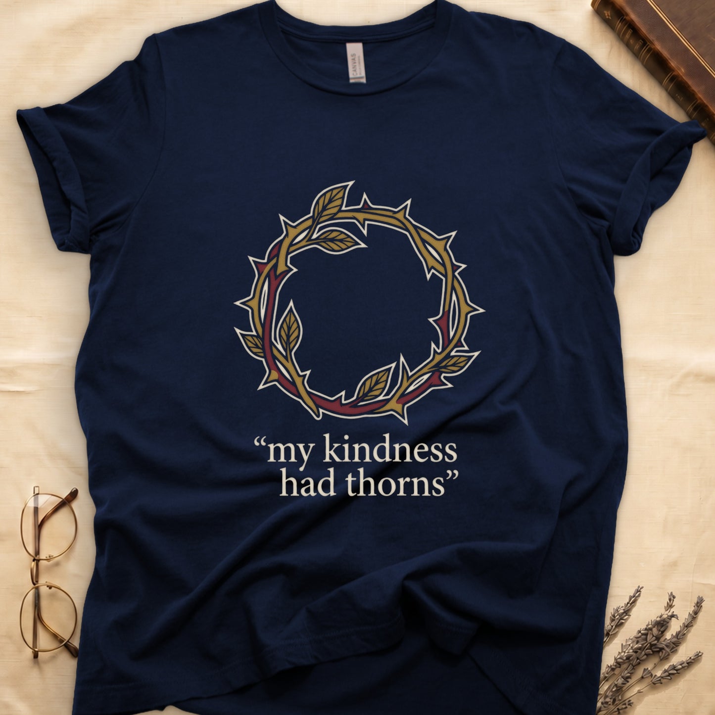 Navy tee with crown of thorns in gold and red with green leaves, "my kindness had thorns" in cream serif.
