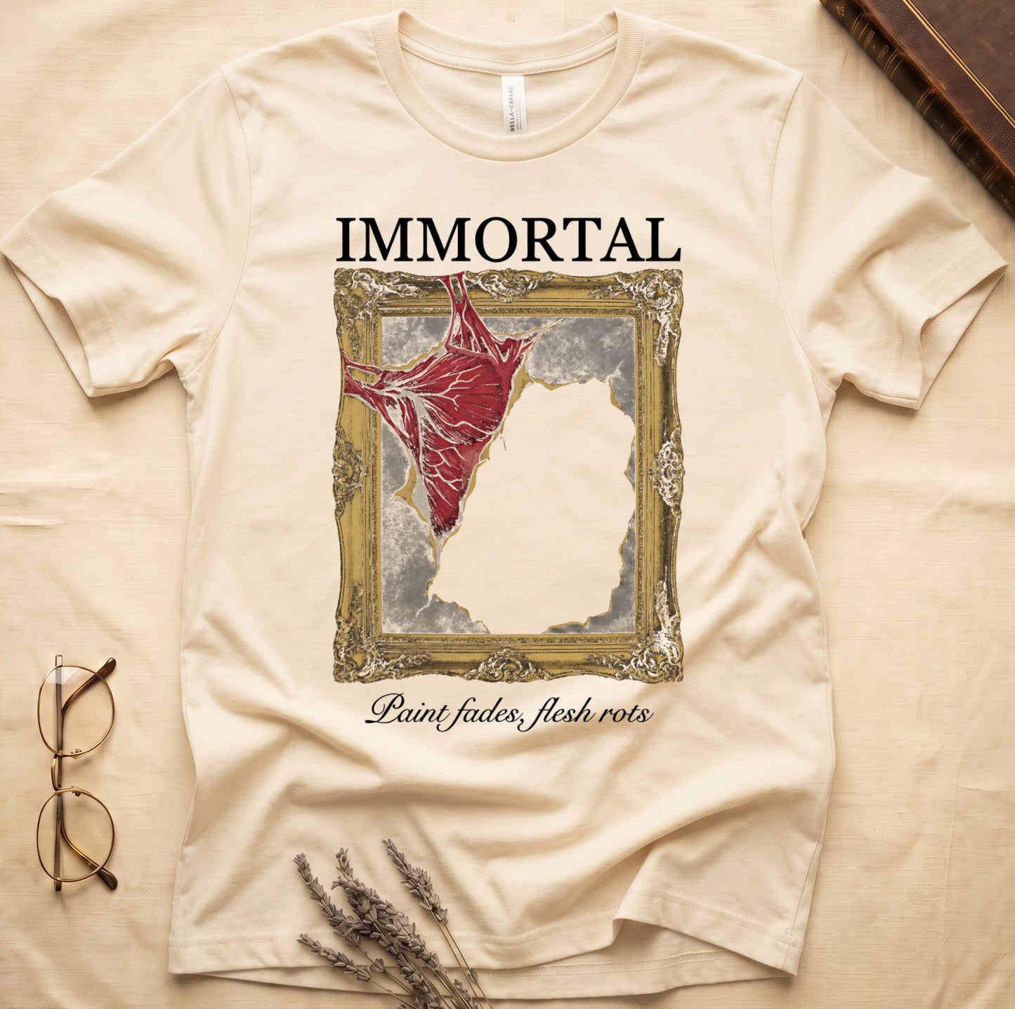 Natural tee with gold frame and exposed muscle tearing canvas, "IMMORTAL" top, "Paint fades, flesh rots" italic below.