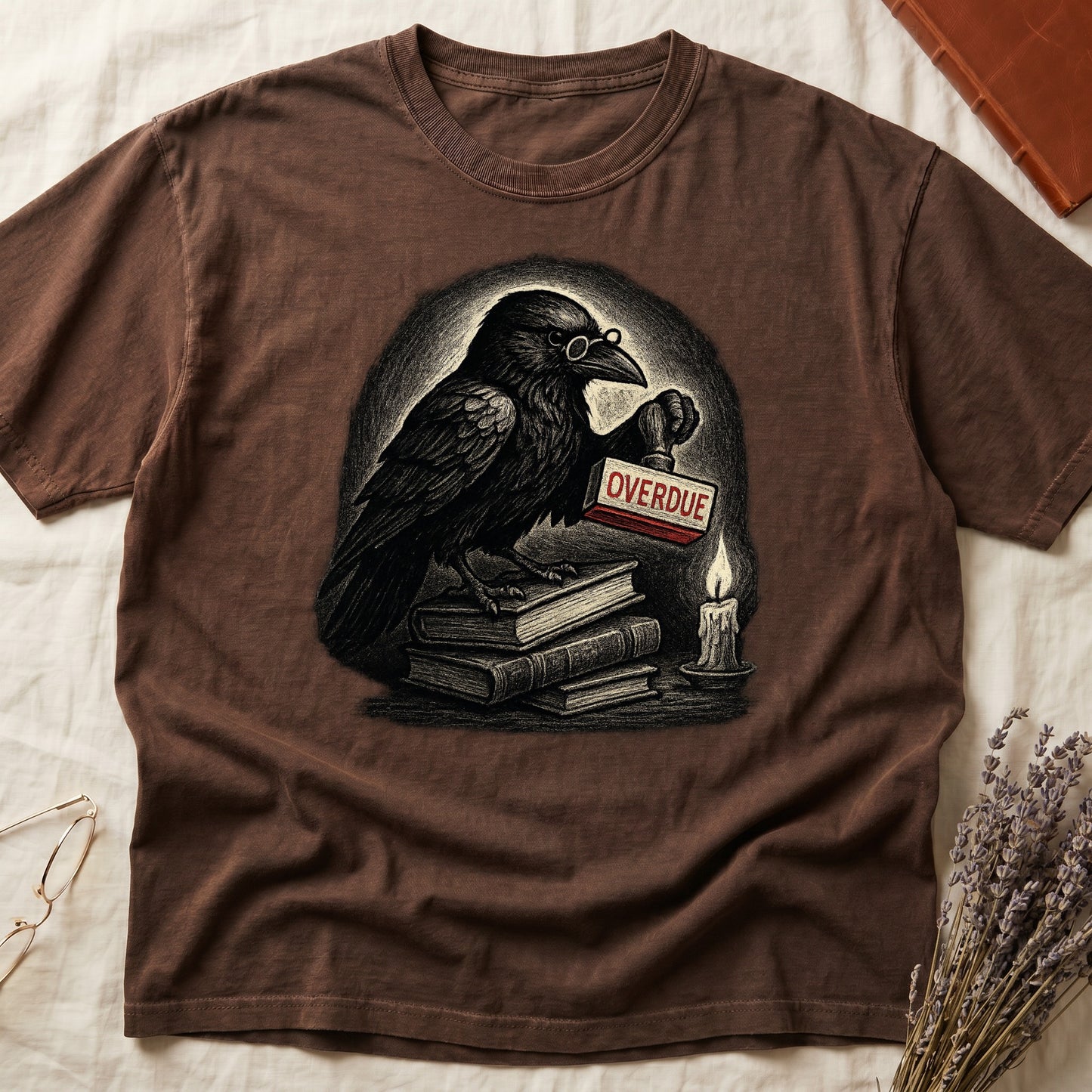 Espresso tee with bespectacled raven on stacked books, holding wooden "OVERDUE" stamp, lit candle beside, dawn glow behind.