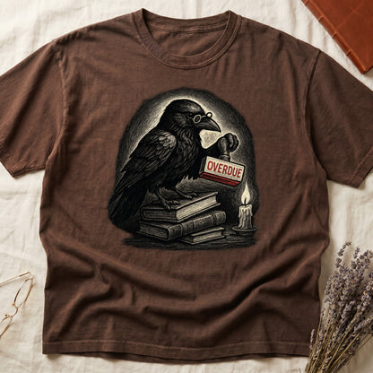 Espresso tee with bespectacled raven on stacked books, holding wooden "OVERDUE" stamp, lit candle beside, dawn glow behind.