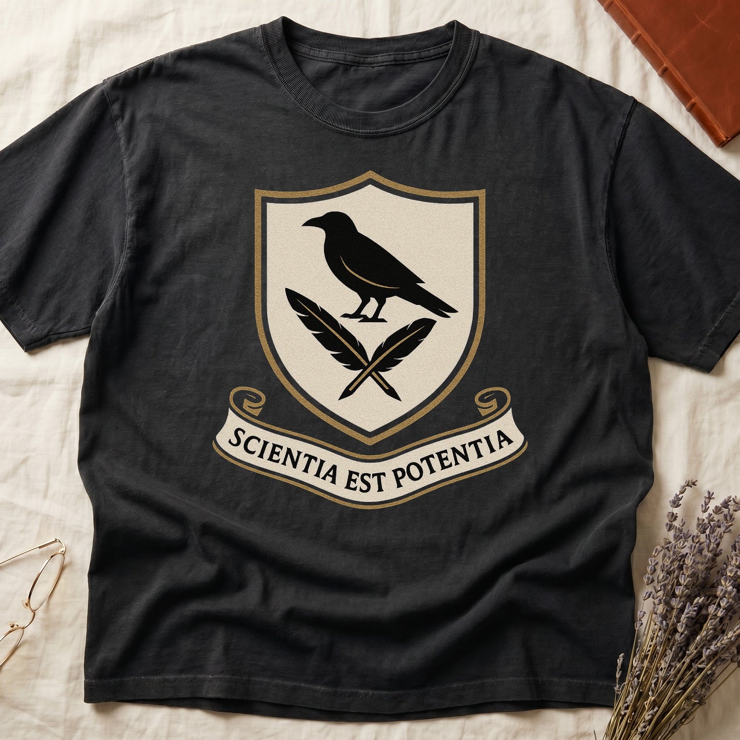 Black tee with cream-and-gold heraldic shield, black raven over crossed quills, scroll banner "SCIENTIA EST POTENTIA" below.