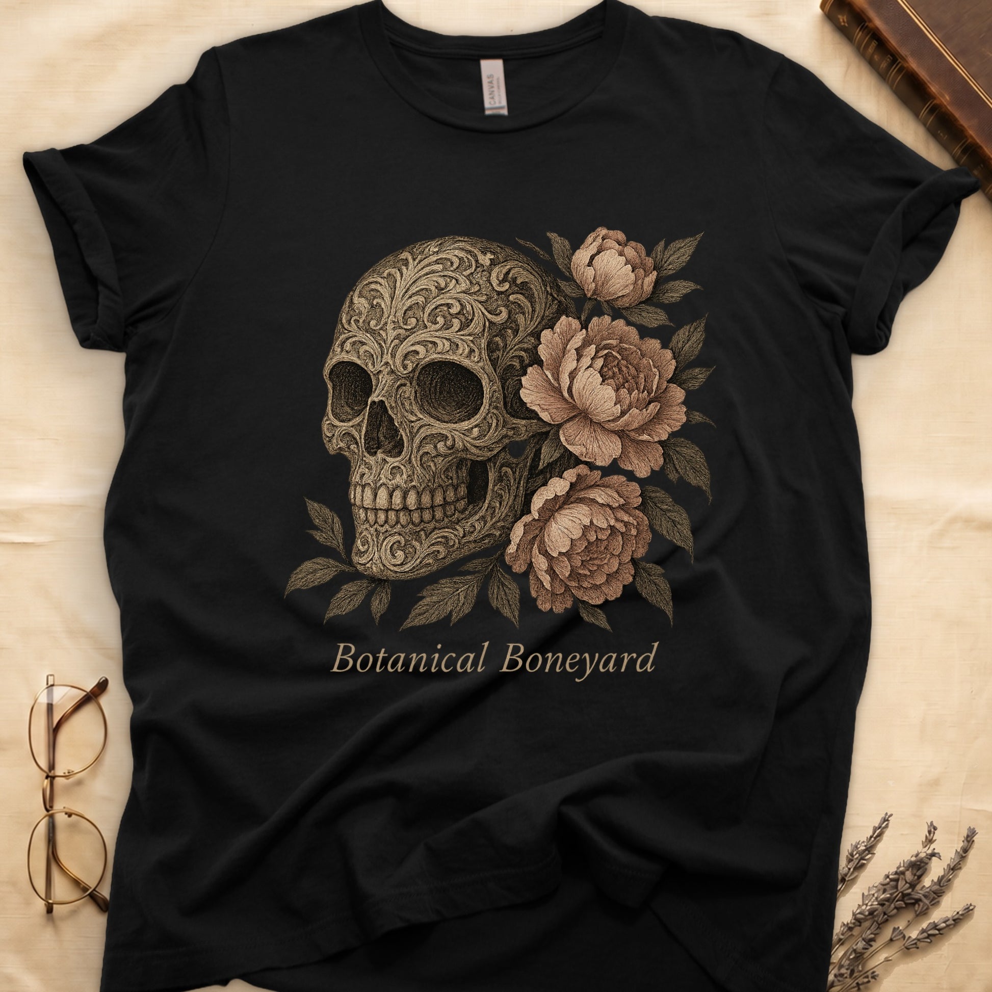 Black tee with filigree-engraved skull on left, peach-cream peonies on right, crossed bones below, "Botanical Boneyard."