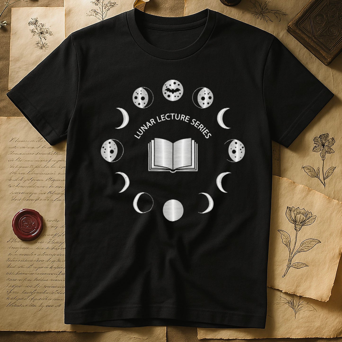 Black tee with open book at center, ring of cream moon phases around, curved "LUNAR LECTURE SERIES" double-arc above.
