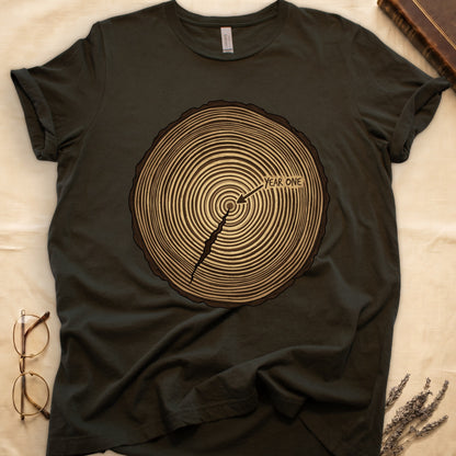Military Green tee with cross-section of tree rings in warm brown, arrow pointing to center labeled "YEAR ONE" in serif type.