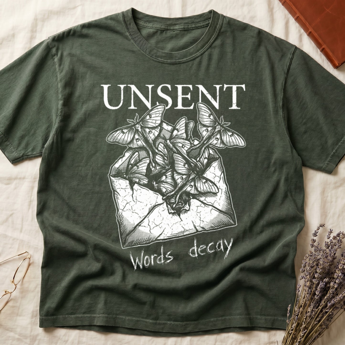 Green tee with 'UNSENT' in serif type, 'Words decay' brush text, luna moths from torn envelope in crosshatched ink