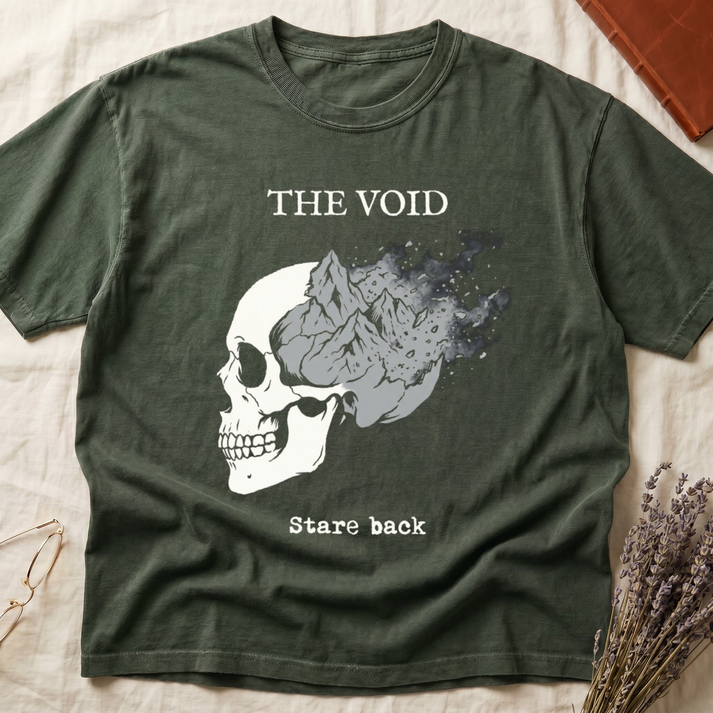 Green tee with skull eroding into mountain landscape and stardust, "THE VOID" top, "Stare back" typewriter below.