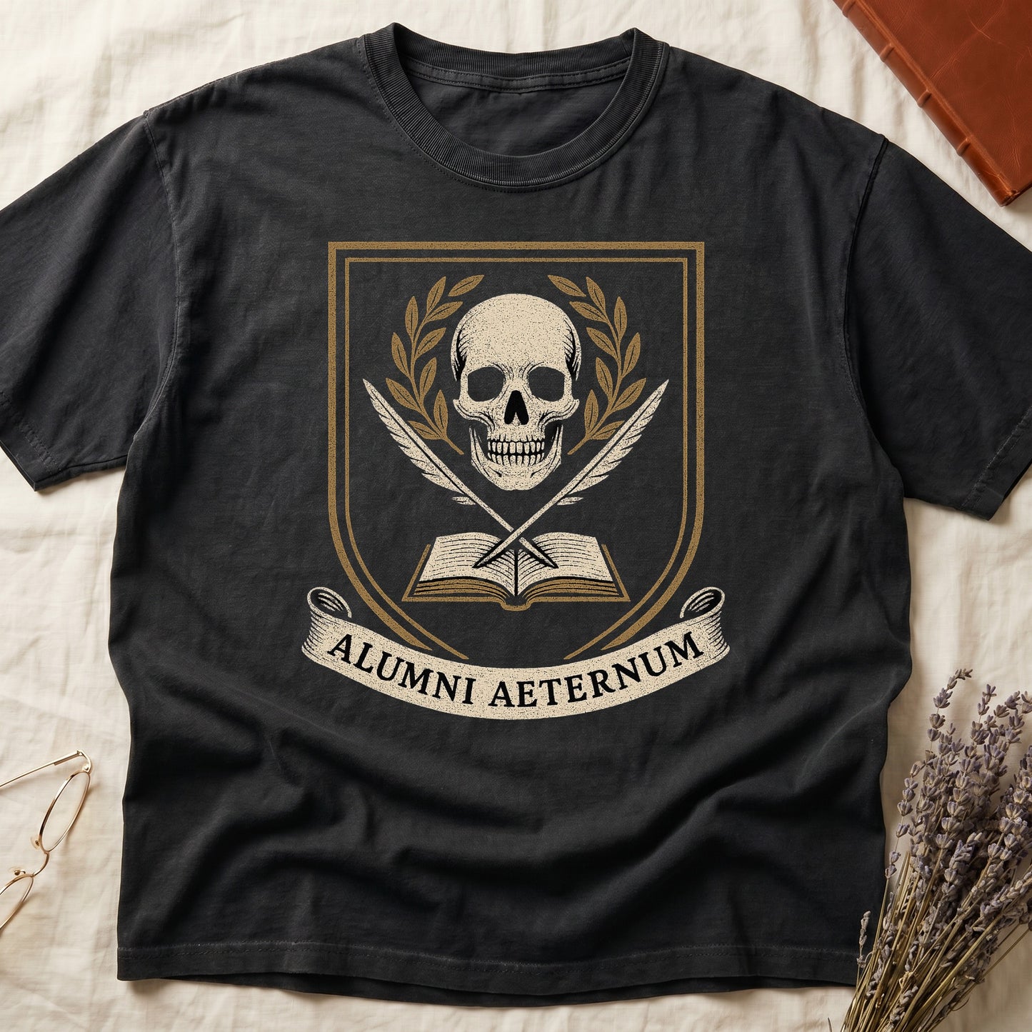 Black tee with heraldic shield, skull and gold laurels, crossed quills, open book, scroll "ALUMNI AETERNUM" below.