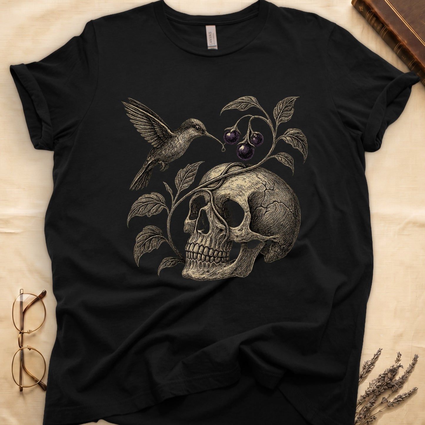Black tee with sepia engraved skull, nightshade vine and dark-purple berries wrapping around, hummingbird at upper left.