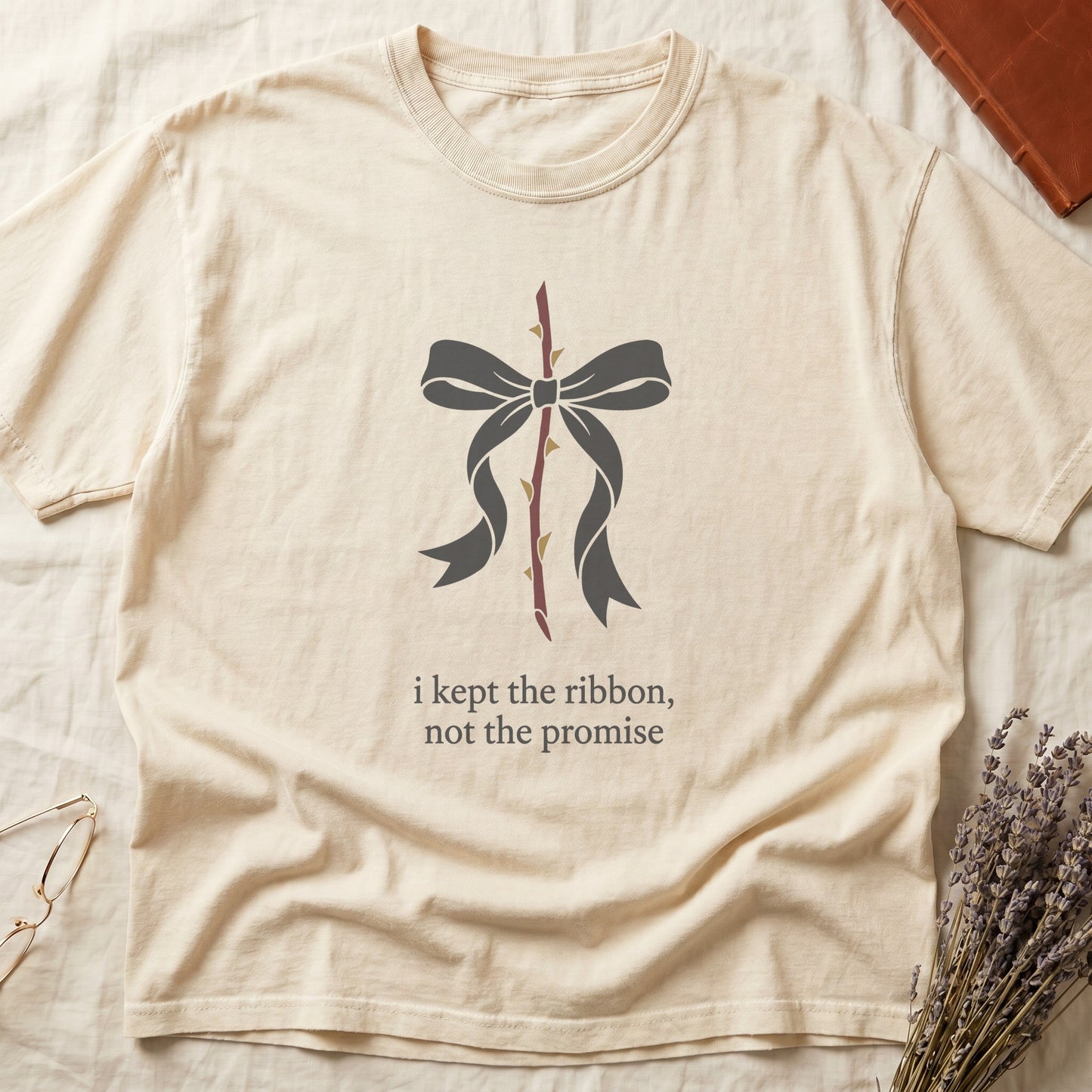Ivory tee with cream bow tied around thorny rose stem, "i kept the ribbon, not the promise" in cream serif below.