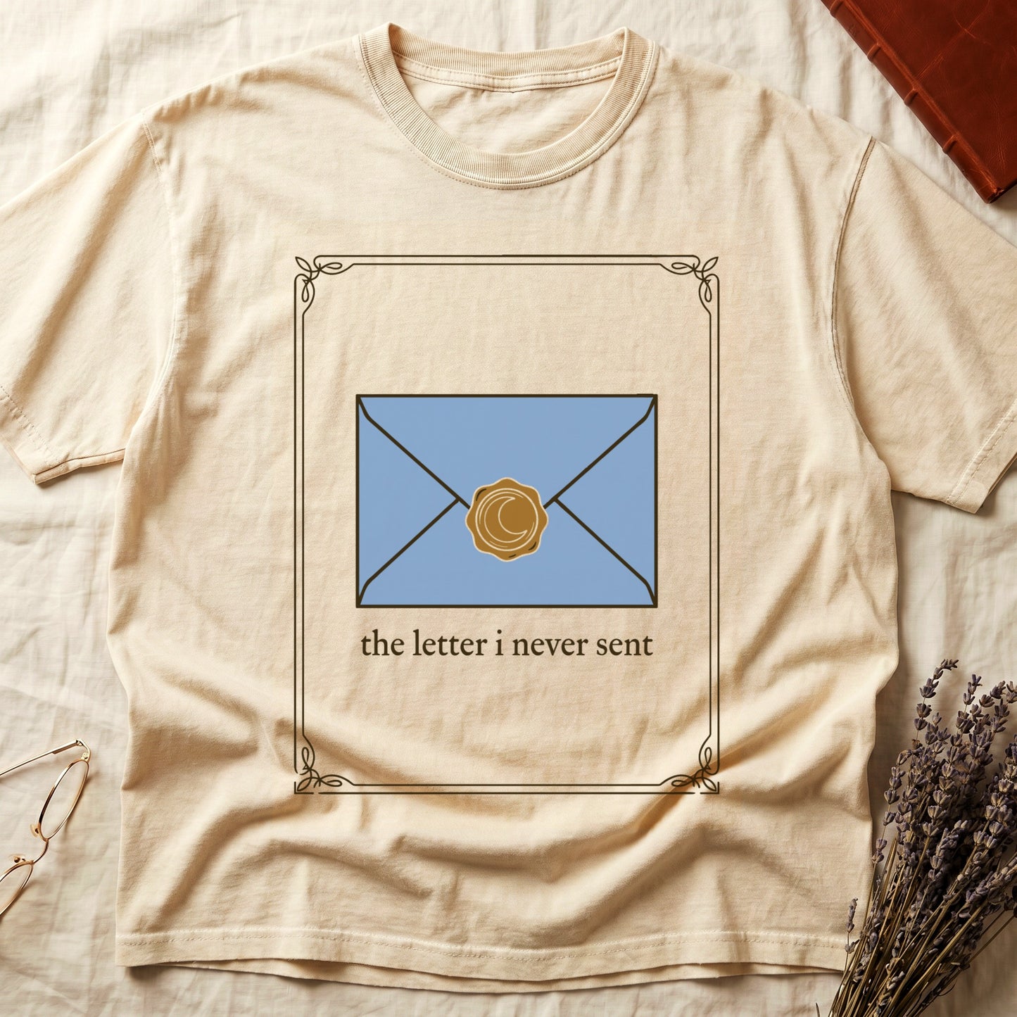 Ivory tee with pale blue envelope sealed with gold crescent moon wax seal, "the letter i never sent" cream serif below.